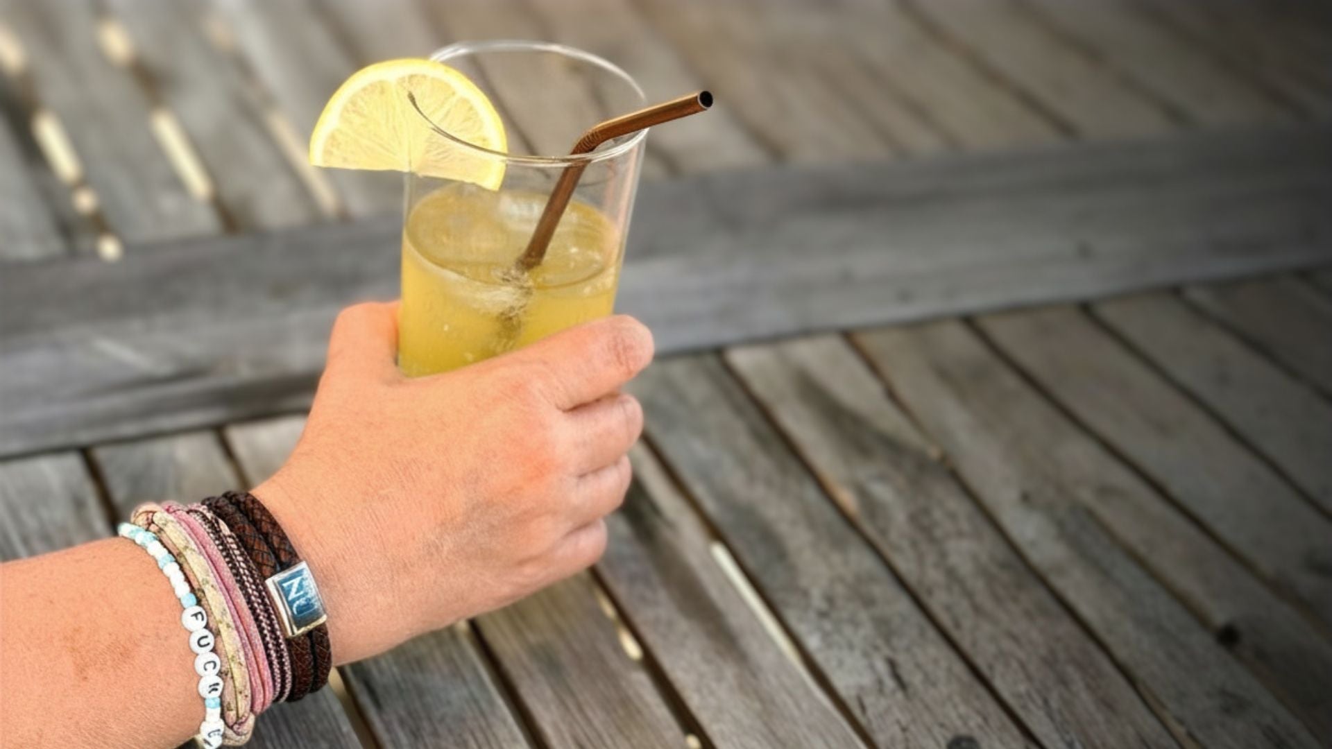 Handled med Livet är nu-armband och andra insamlingsarmband bredvid sommardrink på träbord
